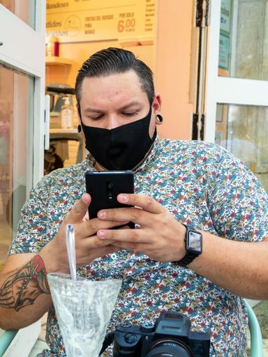 A vertical shot of a male with a medical mask taking a photo of his table at a cafe