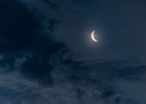 A beautiful shot of a half moon illuminating a dark blue cloudy sky