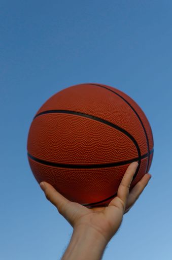 A closeup of red basketball in a man's hands with clear blue sky background