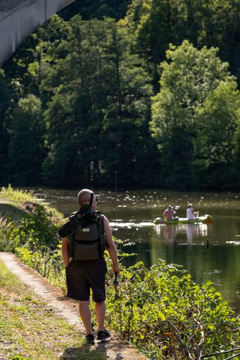A vertical shot of a senior from behind holding a fishing rod and walking near the pond in Loket
