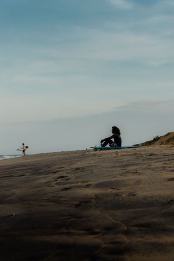 A vertical shot of a surfer resting on the beach with blue sky in the background