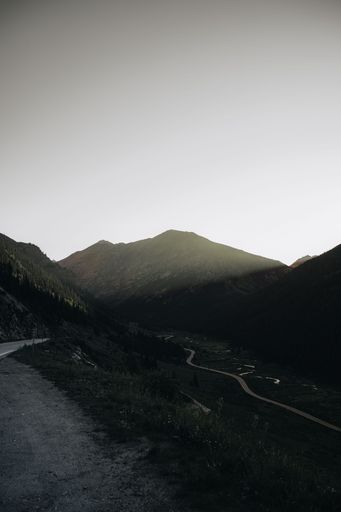 A vertical grayscale shot of mountains and a road in the middle of the range