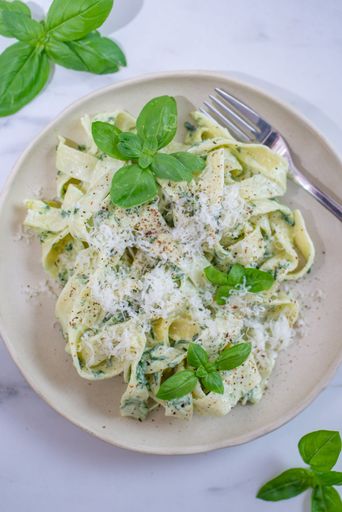 A vertical shot of a plate of pesto pasta with basil and parmesan cheese on the table