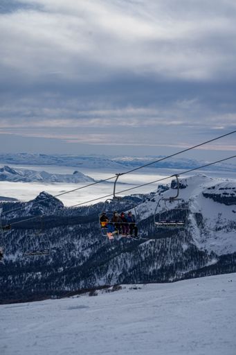 A vertical shot of people on a cable car with a background of snowy mountains