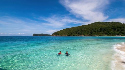Two children swimming in the sea together in a sunny day with mountains in the background