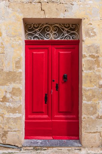 A vertical shot of red wooden door with black handle and knocker of stone building in Valetta, Malta