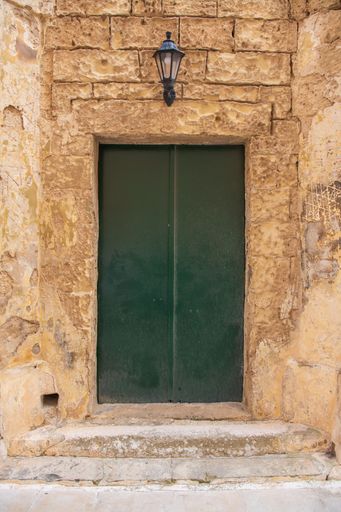 A vertical shot of a green door with steps, and a light at the top