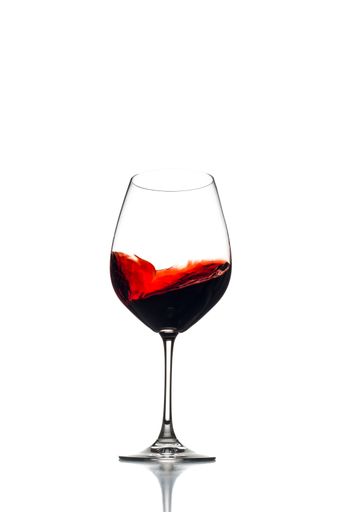 A vertical closeup shot of a wine glass with the red wine swirling inside on a white background