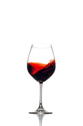 A vertical closeup shot of a wine glass with the red wine swirling inside on a white background