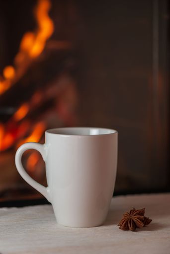 A vertical shot of a white glass mug with a cookie on the side placed on a table