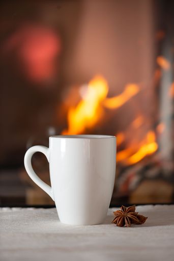 A vertical shot of a white glass mug with a cookie on the side placed on a table