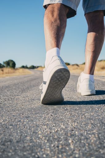 A Vertical shot of a person in white trainers jogging under the sunlight and a blue sky