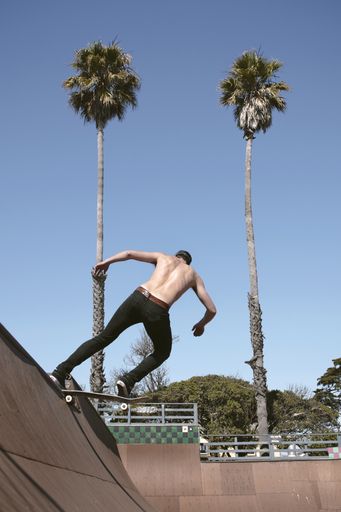 A shirtless male riding on a skateboard doing a trick outdoors during daytime