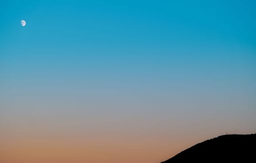 The moon in the sky during a beautiful sunset with a mountain silhouette below