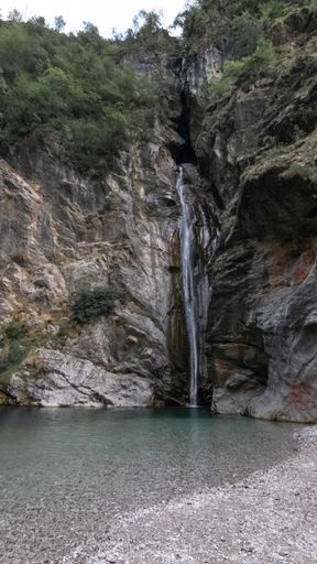 A vertical closeup shot of a scenic waterfall coming out of the hill in the lush forest