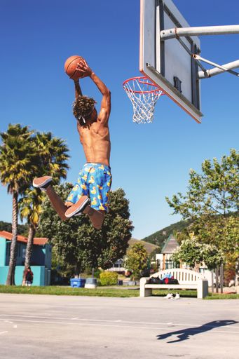 A male with blue and yellow shorts making a dunk in the basketball court during daytime