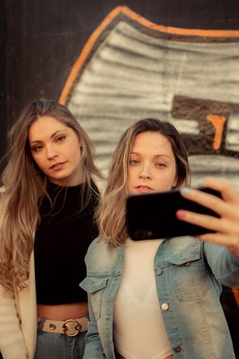 A vertical shot of two female friends taking a selfie against a graffiti