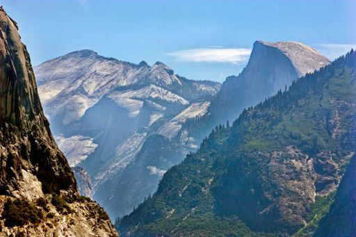 An aerial view of a mountain peak, and rocky mountain slope covered by low vegetation, on a sunny day, with the mountain range in the background