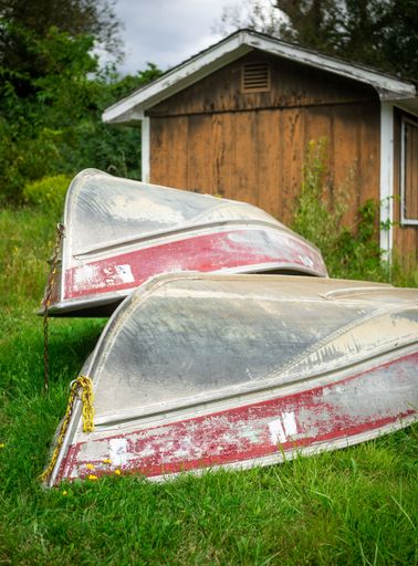 A vertical shot of two old boats on a grass ground in front of the small wooden countryside house