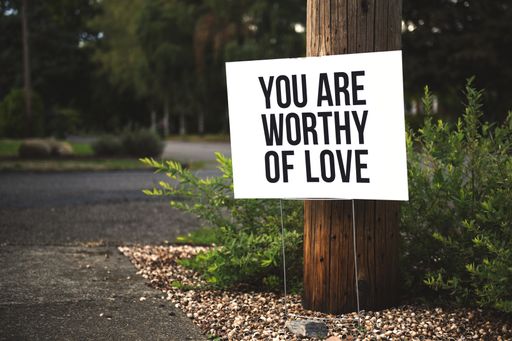 A closeup shot of You are worthy of love signage in front of a tree log near the road