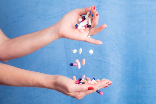 Several pills falling from one hand to another against blue background. Medical supplies.