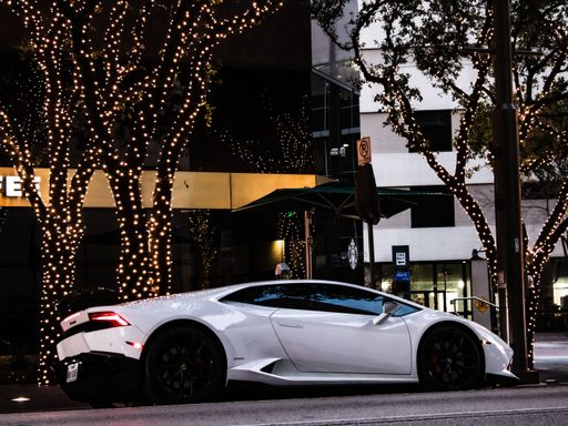 The white Lamborghini parked on side of the downtown street with trees decorated with bokeh lights.