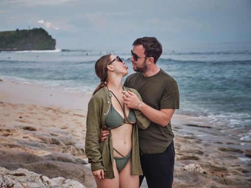 A loving couple posing at the sandy beach with the blue sea and the sky in the background