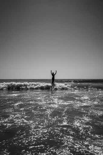 A vertical grayscale shot of a Caucasian female surfing at wavy sea in Cadiz