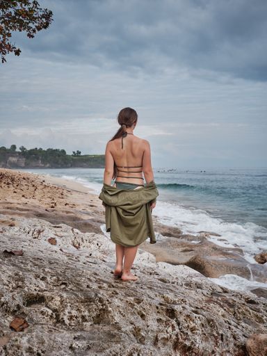 A pretty Caucasian woman in a swimsuit posing at the sandy beach with the blue sea in the background