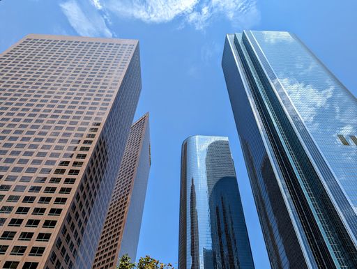 A low-angle shot of skyscrapers in Los Angeles with blue sky and clouds reflecting in windows