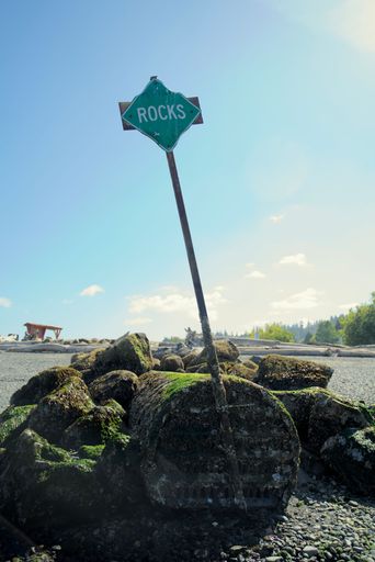 A vertical shot of a green sign with the text rocks on a beach