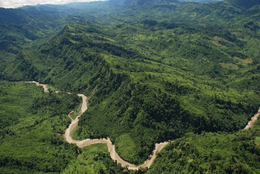 A bird's eye view of a road in mountains covered with green forests under a cloudy sky