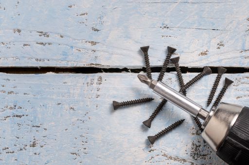 black screws and a the top of s cordless screwdriver on a wooden blue background with copy space