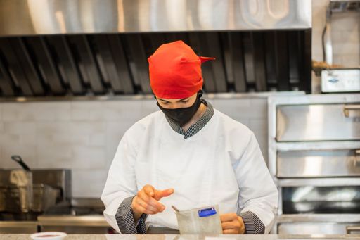 A shallow focus of a young cook with a facemask working in front of a kitchen counter