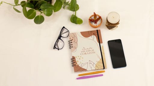 A flat lay of a diary with Dream with all your heart text in Spanish, with eyeglasses, pens, and phone