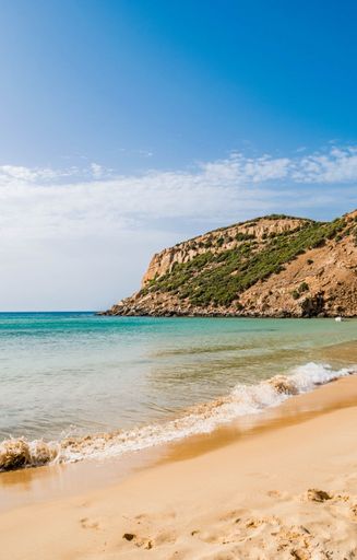 A vertical shot of a sunny rocky seashore with a cliff on a summer day in Kef Abbed, Tunisia