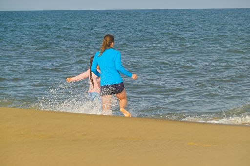 A Caucasian woman running into sea waves at Bethany Beach with her girl in Delaware