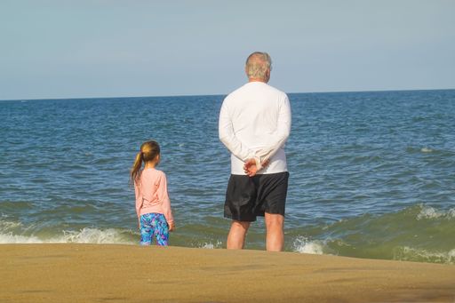The Grandfather and granddaughter looking at the sea horizon from the beach in Bethany Beach, DE