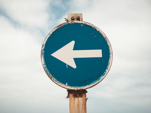 A closeup shot of a rusty blue and white arrow pointing in a left direction