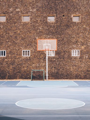 A vertical shot of an empty basketball pitch with a brown building on the background