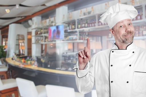 A portrait of a cheerful cook chef with a cafeteria on the background - cooking concept