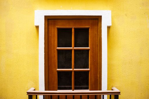 A closeup shot of a wooden door with windows on a yellow wall - great for a cool background