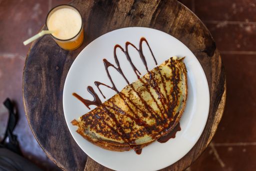 A high angle shot of delicious chocolate-covered crepe and an orange juice on a wooden table