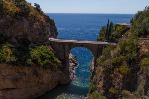 A high angle shot of an arch bridge connecting high rocky mountains near the sea