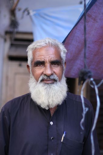 A vertical portrait of a Pakistani old male with a white beard in a kurta standing in the street