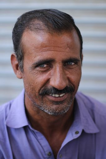 A portrait of a Pakistani middle-aged male with a mustache smiling