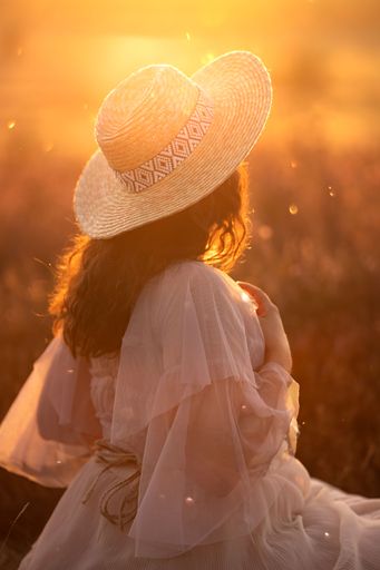 A vertical shot of a woman in a white dress and a hat at sunset.