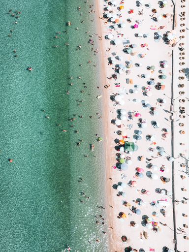 An aerial top shot of a sandy beach with people and sea waves approaching the coast