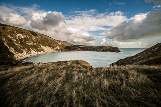 A scenic view of a lake surrounded by a small hill on a cloudy day