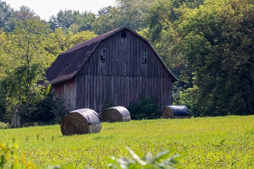 A barn captured in a countryside with covered hays in front of it